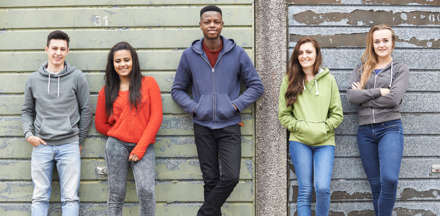 Five teenagers leaning against a wall