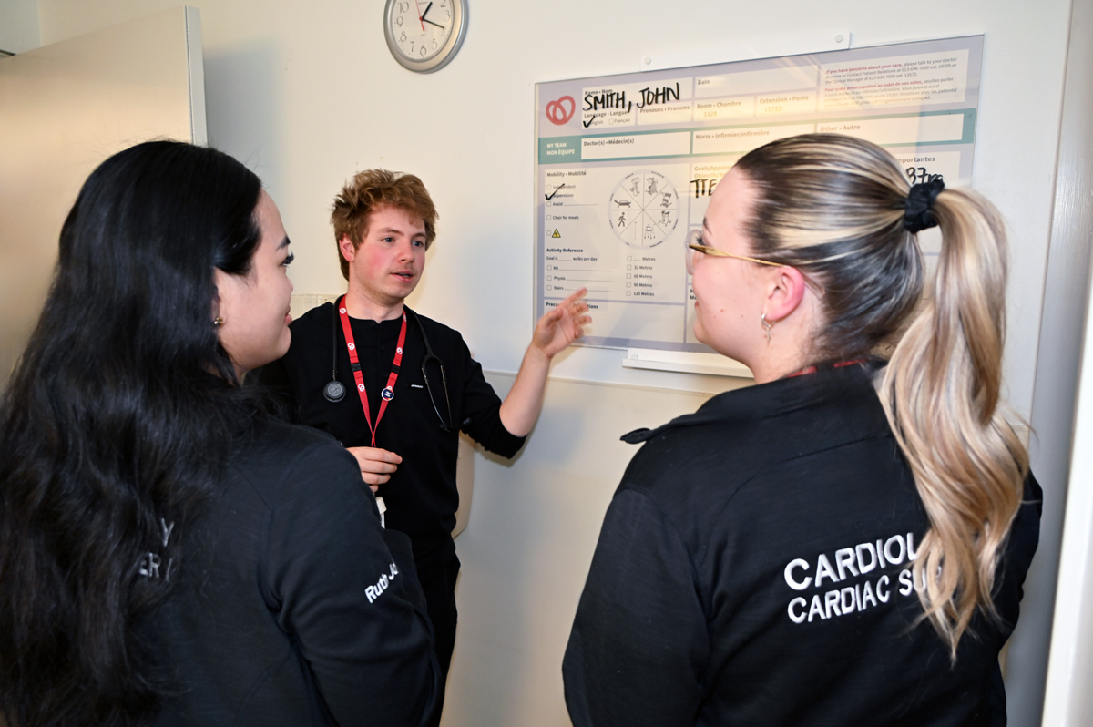 Nurses James Magro, Ruth Martin Joy Ramos, and Natalia Artukovic review key patient information on the whiteboard during a team huddle.