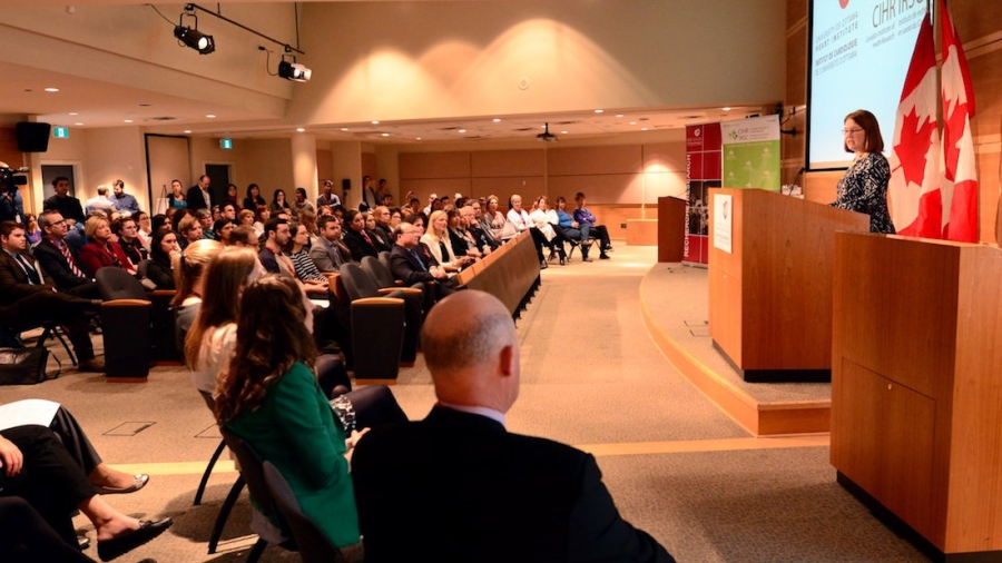 The Minister of Health standing at a podium, in front of a crowd in an auditorium