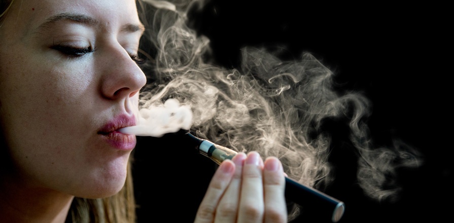 Une femme utilise une cigarette électronique. Un nuage de vapeur sort de sa bouche.