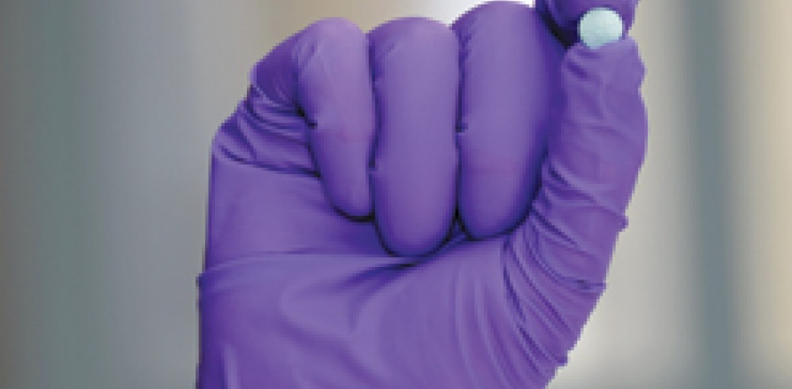 A gloved hand holding a blue pill